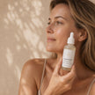 Woman holding Silver Rose Skin Rescue Serum against cheek against a warm beige background representing best Australian skincare for  with directions for Australian skin.