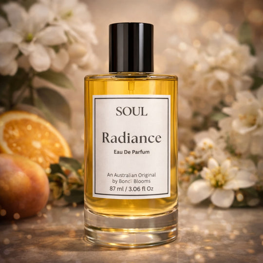Perfume bottle labeled 'Soul Radiance' aromatherapy perfume made with essential oils with flowers and fruit in the background representing premium essential oils in the Australian original perfume.