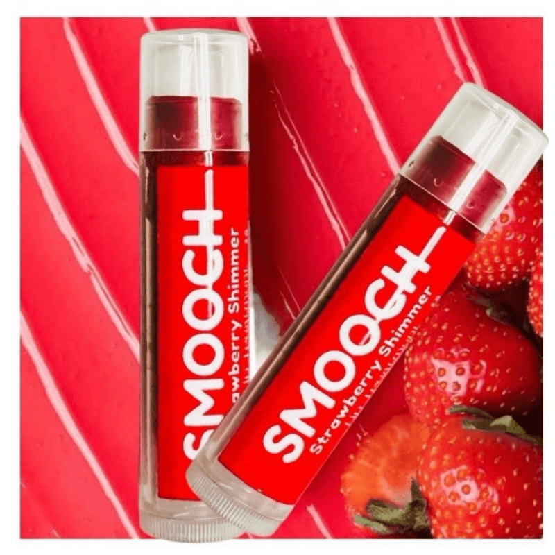 Two Strawberry Tinted Lip Balm tubes with fresh strawberries on a red background