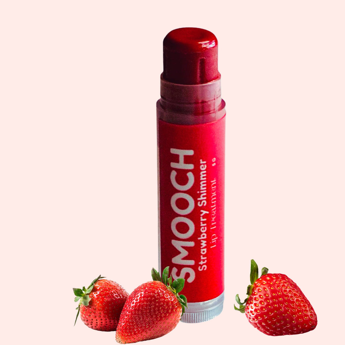 Strawberry lip balm on clean white background with fresh strawberries representing clean natural lip care.