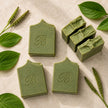 Flat lay of handmade green sulphur soap with plantain and comfrey, showing stamped bars and natural botanical texture.