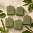 Four handmade sulphur soap bars with plantain and comfrey on a warm ivory background with botanical leaves.