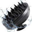 close up of black silicone scalp massage brush with soft bristles against white background and splash of water representing natural australian haircare essentials.