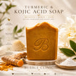 A bar of turmeric and kojic acid soap by Bubble Clinic, displayed on a wooden stand with turmeric roots, white powder, and white flowers in a softly lit natural setting representing best turmeric kojic soap australia.