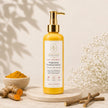 A bottle of Bubble Clinic Brightening Foaming Cleanser with a gold pump and white label, styled on a marble coaster with turmeric roots, powder, and dried flowers on a warm beige background.