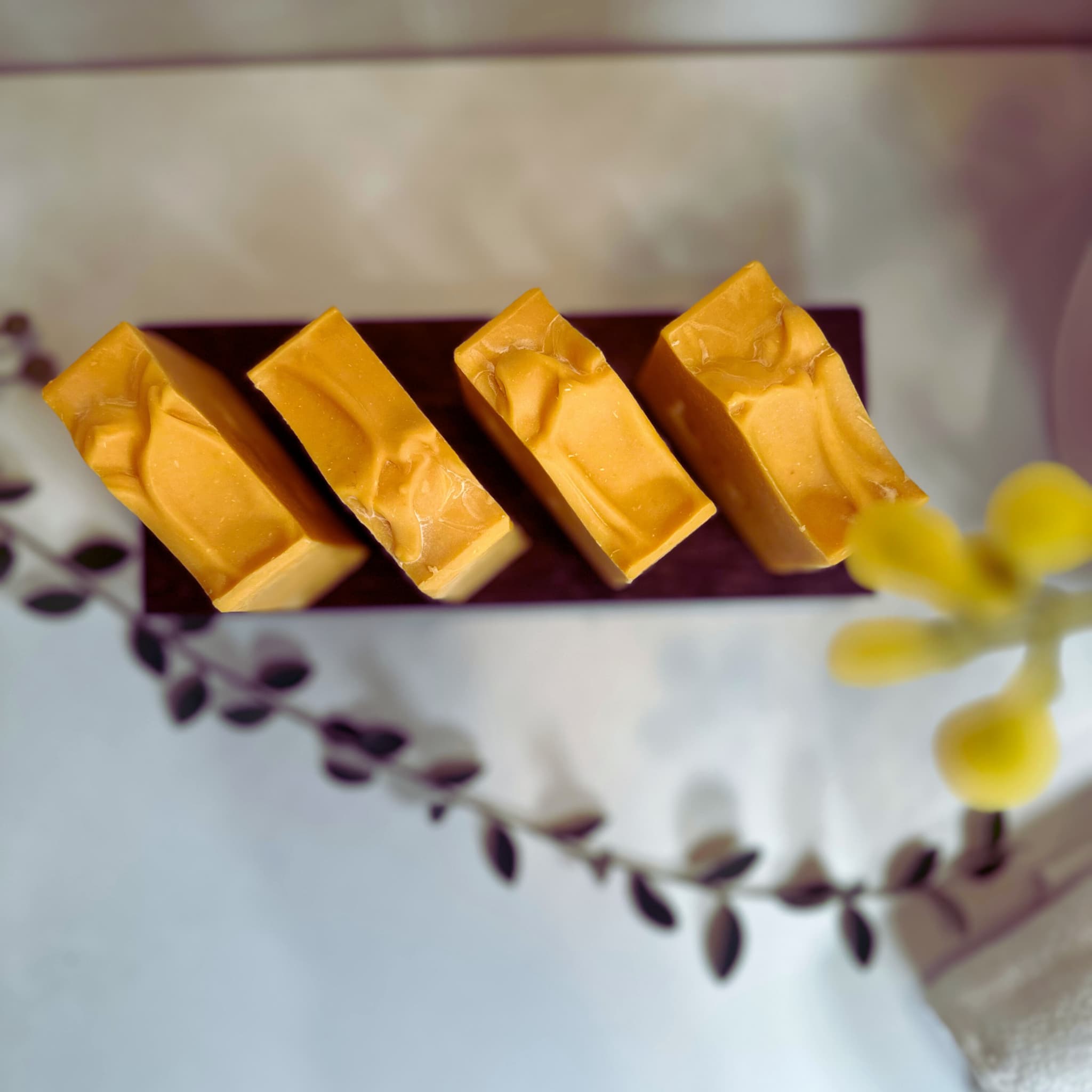 close up top view of 4 organic brightening, bright yellow, kojic turmeric soap bars with botanicals in the foreground. 