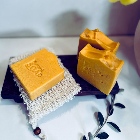 close up front and side view of bright yellow, brightening turmeric kojic acid soap for acne scars and dark spots with botanicals in the foreground  representing natural Australian Skincare. 