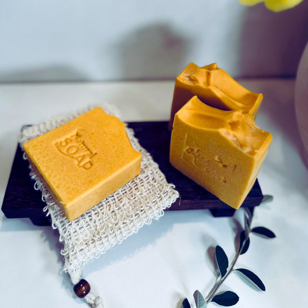 close up front and side view of bright yellow, brightening turmeric kojic acid soap for acne scars and dark spots with botanicals in the foreground  representing natural Australian Skincare. 