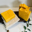 close up of 3 bright orange, yellow natural carrot turmeric kojic acid soap for dark spots and acne scars with botanical leaves in the foreground representing natural brightening skincare. 