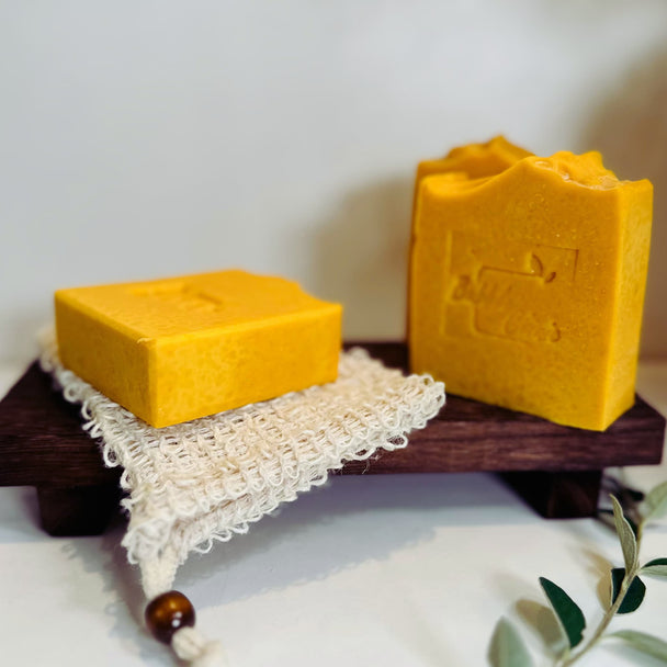 close up front and side view of 3 bright yellow natural brightening turmeric kojic acid soap on rustic wooden surface and natural sisal soap pouch representing natural brightening and cleansing routine Australia. 