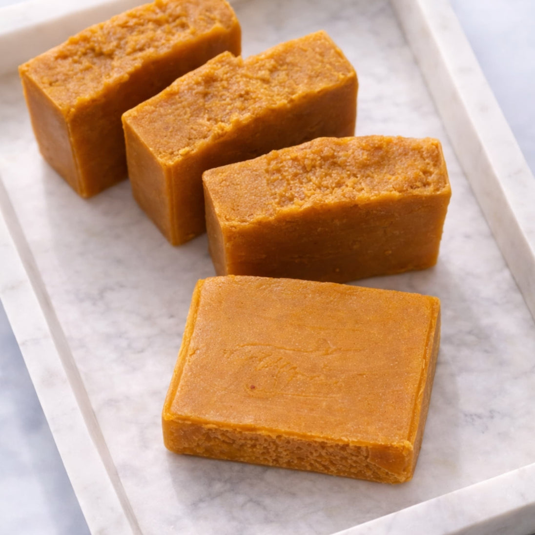 4 hot processed natural brightening Turmeric and Kojic Acid Soap on a white concrete tray for brighter skin and even tone.