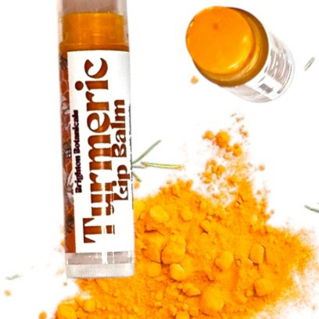 Close up of organic, turmeric lip balm tubes against white background with turmeric powder highlighting clean, natural skincare and lip care.
