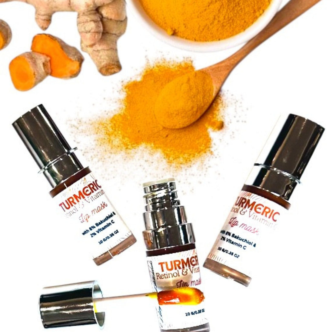 3 luxury lip mask bottles with large applicator. Organic turmeric root and powder against white luminous background representing clean, organic skincare.