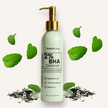 Powerful BHA acne cleanser with zinc pyrithione and Vitamin C in a clear bottle and gold pump revealing creamy light green texture of the cleanser with mint leaves and tea tree in the background highlighting the essential oils to fragrance the cleanser.